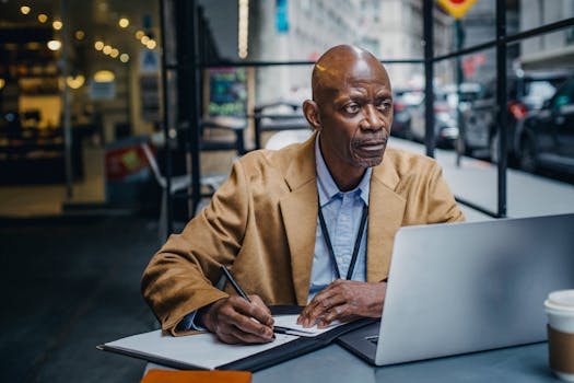 person writing in a notebook with a laptop and coffee